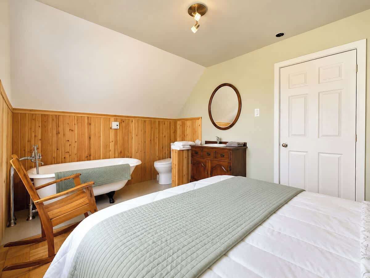A bedroom with a bed, a wooden chair, a bathtub, a toilet, and a dresser.