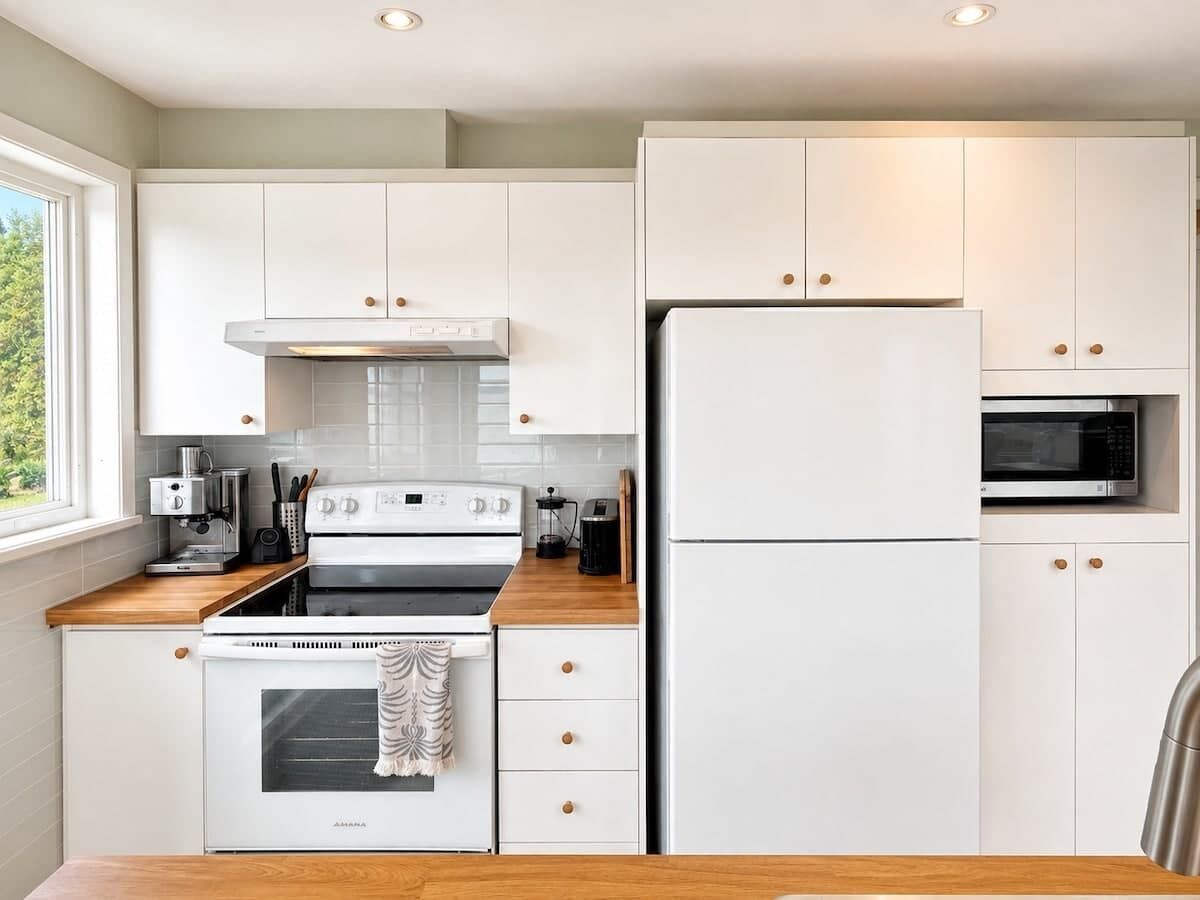 A modern kitchen with white cabinetry, a built-in oven, a refrigerator, and a microwave.