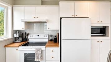 A modern kitchen with white cabinetry, a built-in oven, a refrigerator, and a microwave.