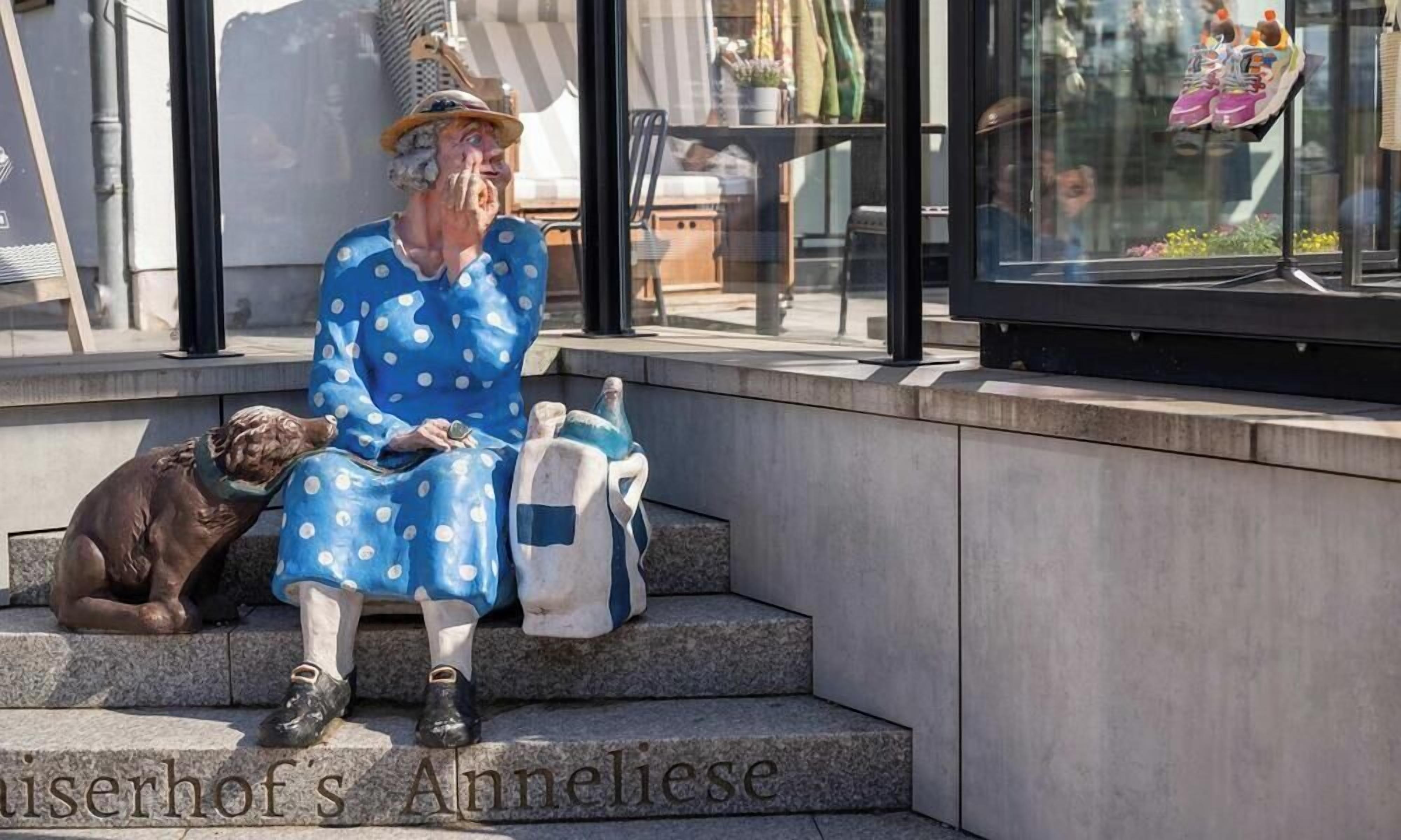 A statue of a woman in a polka dot dress sitting on steps with a dog beside her.