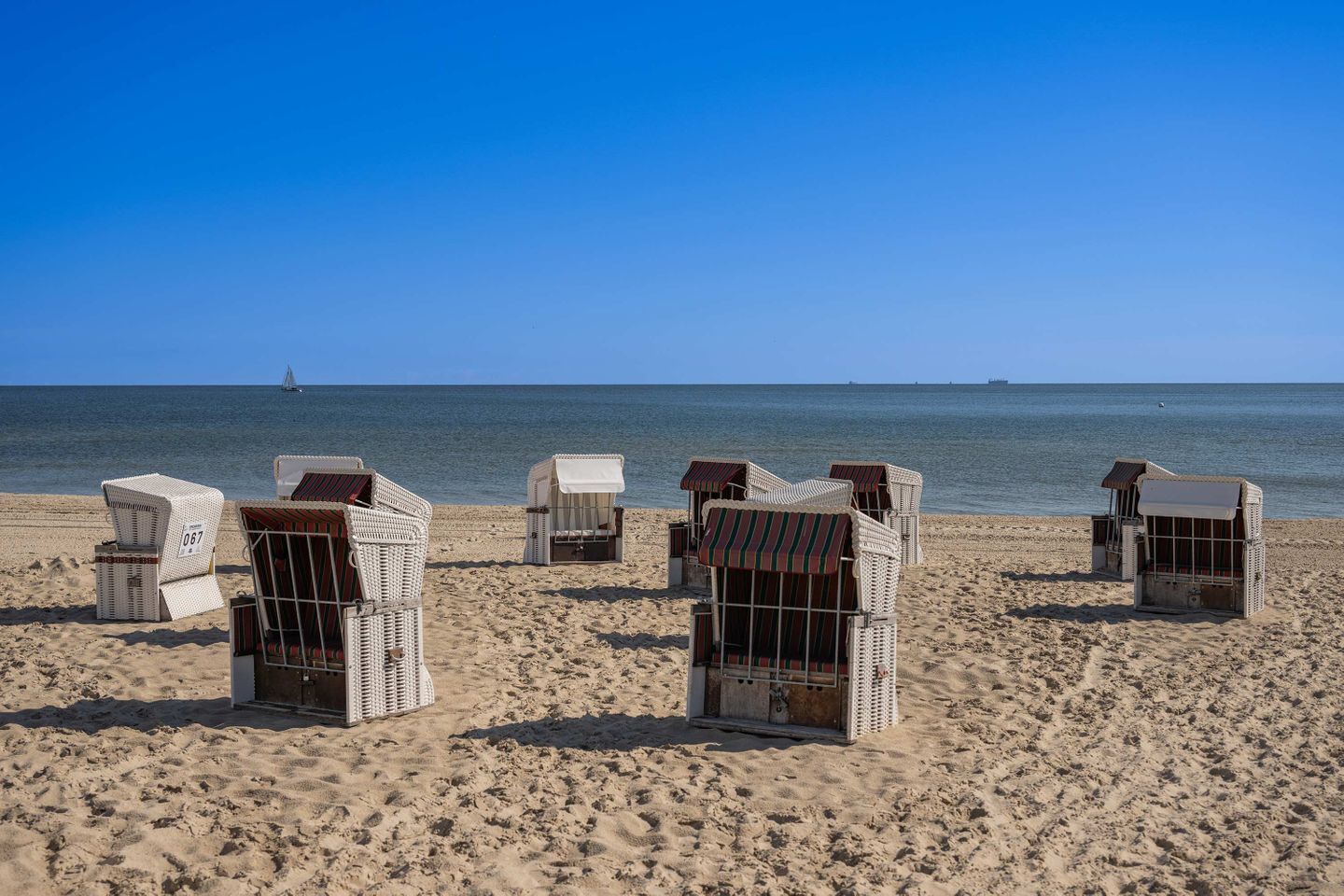 Strandstühle auf sandigem Strand, im Hintergrund das Meer.
