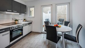 A modern kitchen with a dining area, featuring a built-in oven, a sink, and a dining table with chairs. - Villa Marina, Apartment 03, just 450 m from the beach - Dogs Welcome - Modern (Heringsdorf)