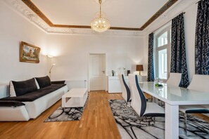 A modern living room with a sofa, coffee table, dining table with chairs, a chandelier, and a view of the city through the window. - Villa Marina, Apartment 02, just 450 m from the beach - Dogs Welcome - Modern XXL (Heringsdorf)