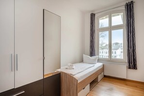 A bedroom with a bed, a wardrobe, and a window with curtains. - Villa Marina, Apartment 01, just 450 m from the beach, with a bathtub and shower - Modern (Heringsdorf)