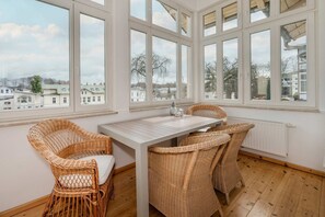 A room with a large window, wicker furniture, and a view of buildings outside. - Villa Marina, Apartment 01, just 450 m from the beach, with a bathtub and shower - Modern (Heringsdorf)