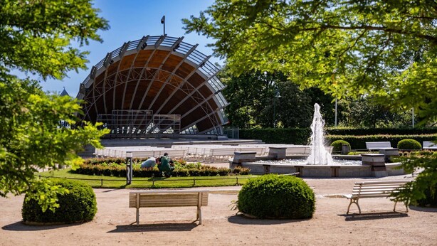 Ein Park mit einem großen, runden Gebäude, einer Fontäne und Bänken.