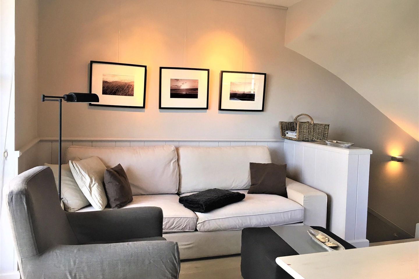 A modern living room with a sofa, a coffee table, and a floor lamp. There are three framed pictures on the wall above the sofa.
