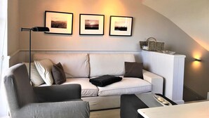 Ett modernt vardagsrum med en soffa, ett soffbord och en golvlampa. På väggen ovanför soffan hänger tre inramade tavlor.