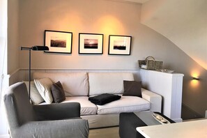 Ein modernes Wohnzimmer mit Sofa, Couchtisch und Stehlampe. Über der Couch hängen drei gerahmte Bilder an der Wand.