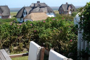 Ein Küstendorf mit reetgedeckten Häusern, einer hölzernen Bank und Blick auf das Meer.