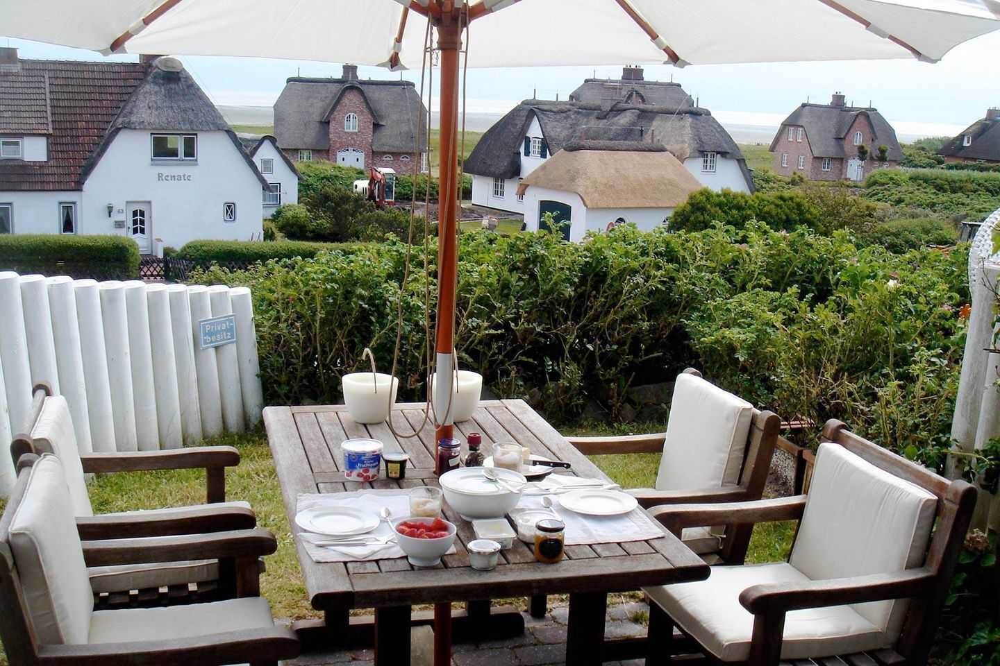 A picnic table set up outdoors with a thatched-roof house in the background.