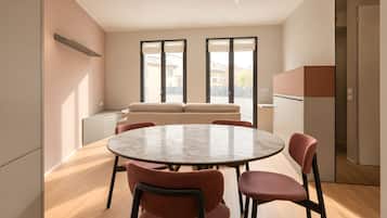 A modern dining area with a round table and chairs, a sofa, and a kitchen in the background.