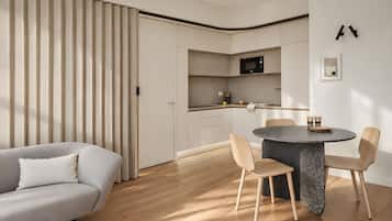 Un salon moderne comprenant un canapé, une table à manger avec des chaises et un coin cuisine avec des placards et un four à micro-ondes.