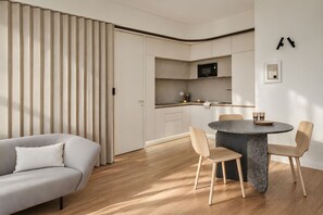 A modern living room with a sofa, a dining table with chairs, and a kitchen area with cabinets and a microwave. - 7 R House (Milano)