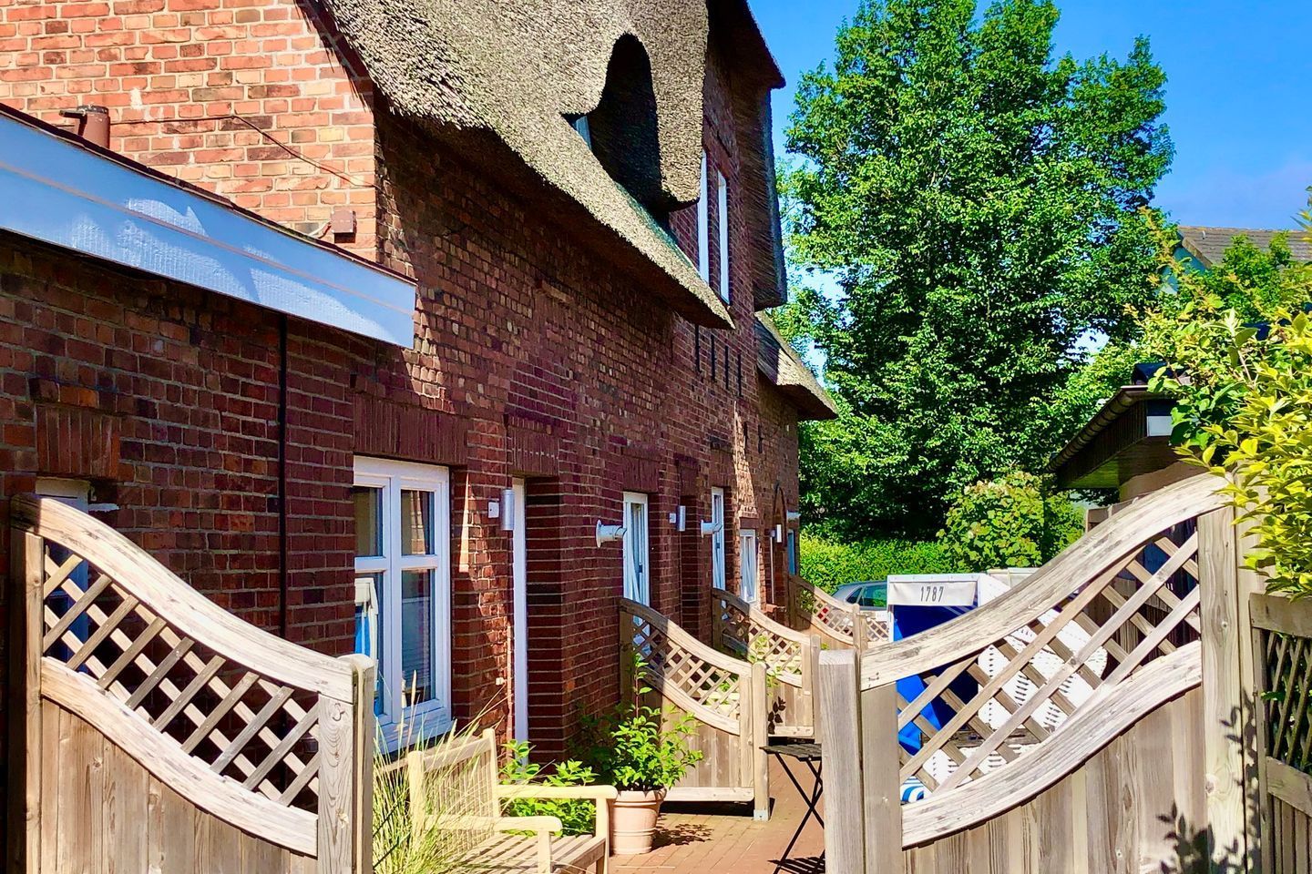 Ein Haus aus Ziegelsteinen mit einem strohgedeckten Dach, hölzernen Toren und einem kleinen Garten.