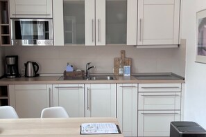 A modern kitchen with a built-in oven, a coffee maker, and a wine bottle on the counter. - Alter Konsumverein, App No. 3 - Cozy apartment in the Alter Konsumverein at (Sylt)