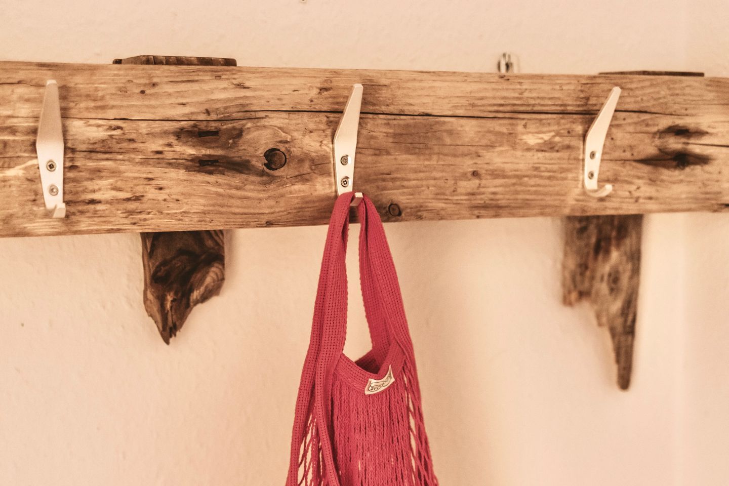 A wooden wall-mounted rack with hooks, holding a red bag.