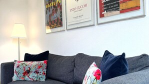 Un divano grigio con cuscini floreali e decorati, una lampada da terra e quadri appesi al muro.