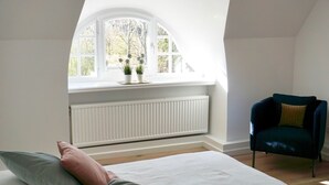 Una camera da letto con un letto, una sedia, una finestra vista alberi e un termosifone.