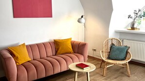 En stue med sofa, rundt sofabord, fletstol, gulvlampe og en radiator.