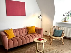 Ein Wohnzimmer mit einer Couch, einem kleinen runden Tisch, einem Korbstuhl, einer Stehlampe und einer Heizung.