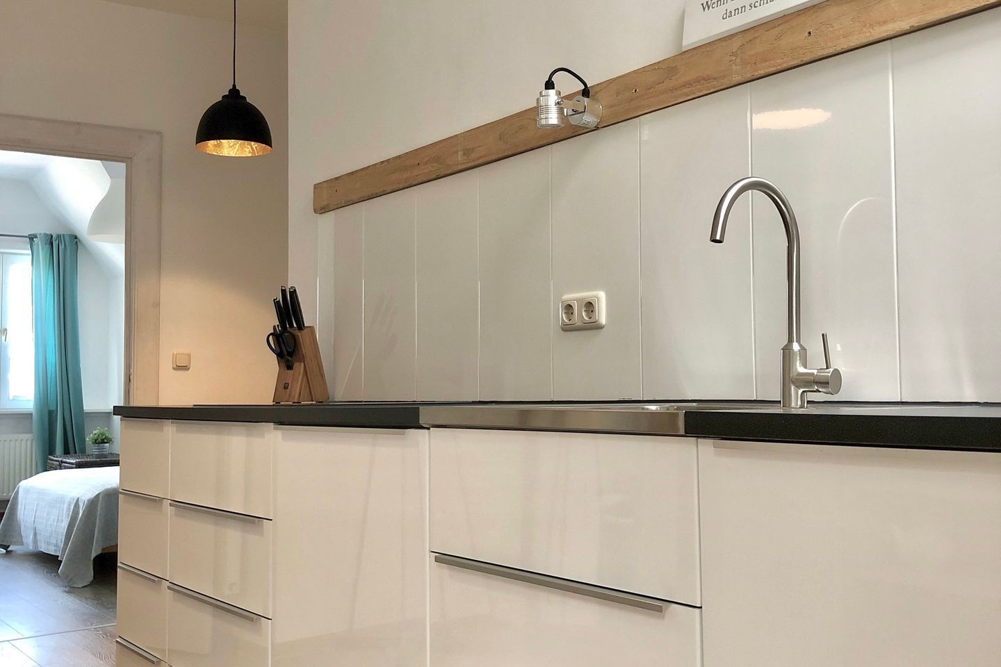 Una cucina moderna con lavello incassato, mensola in legno e lampada a sospensione.