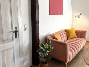 A room with a door, a wall-mounted light, a sofa with cushions, and a potted plant.
