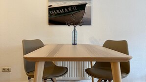 Een eettafel met vier stoelen, een vaas met gedroogde bloemen en een lijst met een foto van een boot aan de muur.