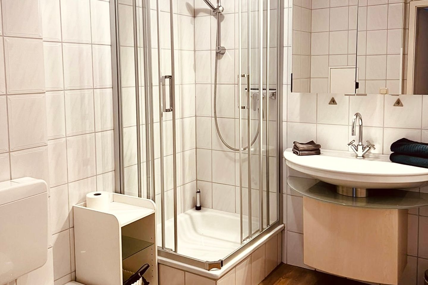 A modern bathroom with a glass-enclosed shower, a white toilet, and a sink with a mirror above it.