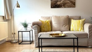 Een woonkamer met een bank, een salontafel, een vloerlamp en een schilderij aan de muur.