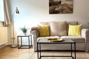 A living room with a sofa, a coffee table, a floor lamp, and a painting on the wall. - Alter Konsumverein, App No. 6 - Cozy Apartment at the Alter Konsumverein on (Sylt)
