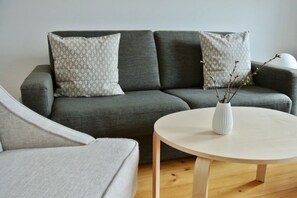 A modern living room with a grey sofa, patterned cushions, a white vase with branches, and a round wooden coffee table. - Alter Konsumverein, App No. 4 - Cozy Apartment at the Alter Konsumverein on (Sylt)