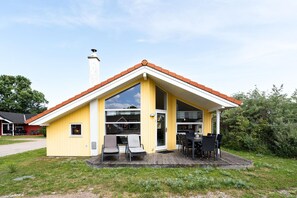 Un bâtiment jaune avec un toit rouge, une terrasse couverte avec des sièges extérieurs et une cheminée.