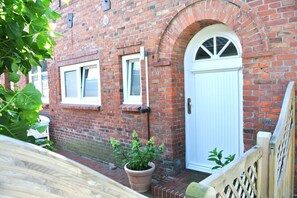 A brick building with a white door and windows, a wooden fence, and potted plants. - Alter Konsumverein, App No. 7 - Cozy Vacation Apartment at Alter Konsumverein (Sylt)