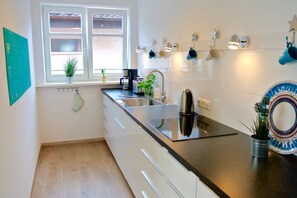 Une cuisine moderne avec un plan de travail noir, des appareils en acier inoxydable, une fenêtre avec des stores et un élément décoratif mural.