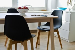 A modern kitchen with a wooden table, two black chairs, and a colander with fruits. - Alter Konsumverein, App No. 7 - Cozy Vacation Apartment at Alter Konsumverein (Sylt)