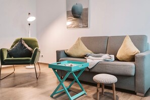 Ein modernes Wohnzimmer mit einem grünen Sessel, einem grauen Sofa, einem türkisfarbenen Couchtisch und einem kleinen Hocker.
