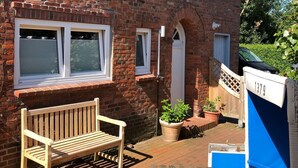 En träbänk, en krukväxt och en brevlåda med nummer 1379 på en uteplats med ett stengolv.