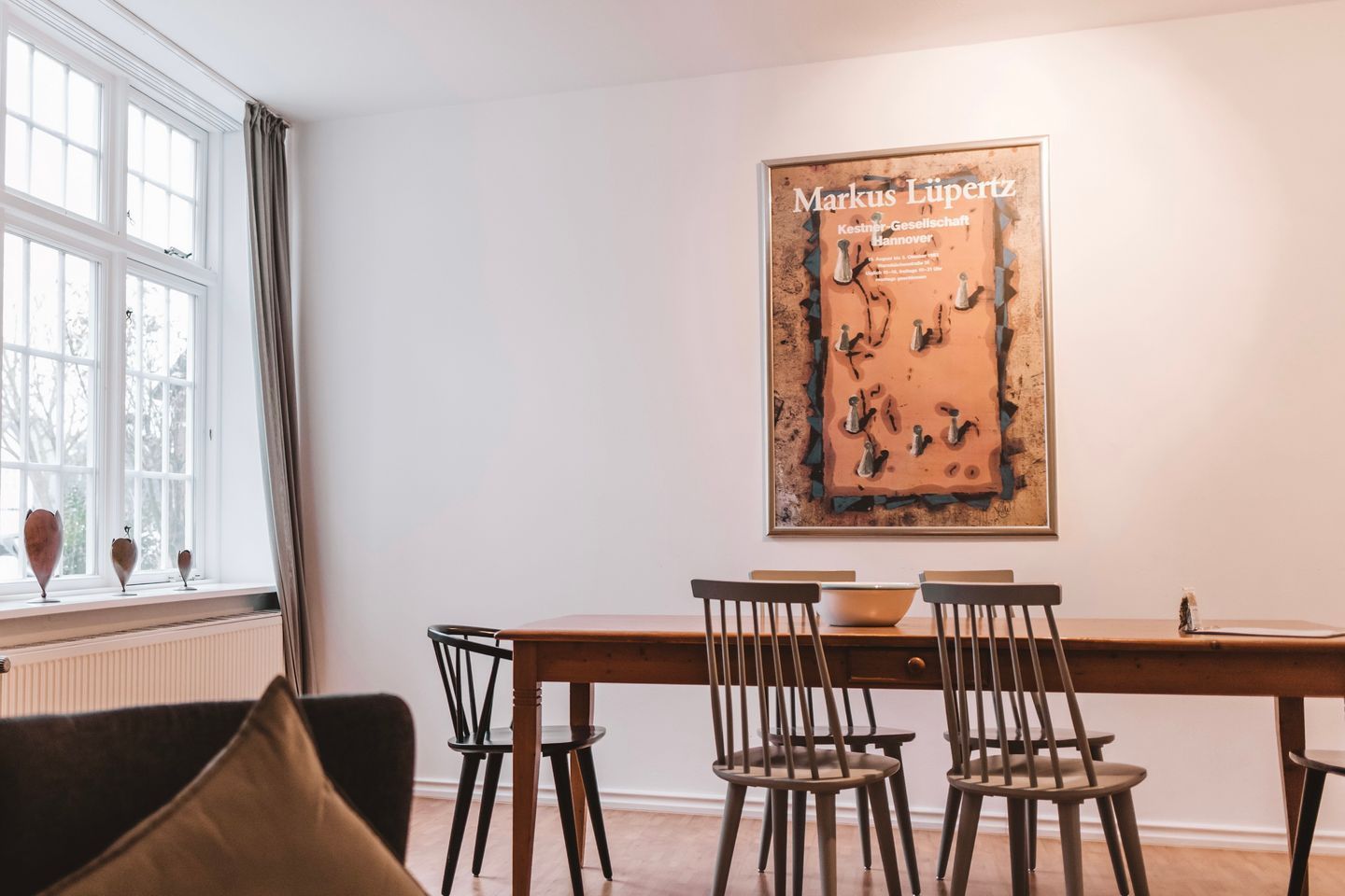 Ein Essbereich mit Tisch und Stühlen, einem Fenster mit Vorhängen und einem gerahmten Kunstwerk an der Wand.