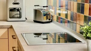 A kitchen with a stainless steel toaster, a coffee maker, and a colorful tiled backsplash. - Alter Konsumverein, App No. 5 — An Oasis of Well-Being: Alter Konsumverein App No. 5 on Sylt (Sylt)