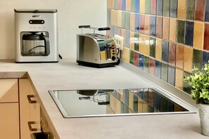 A kitchen with a stainless steel toaster, a coffee maker, and a colorful tiled backsplash. - Alter Konsumverein, App No. 5 — An Oasis of Well-Being: Alter Konsumverein App No. 5 on Sylt (Sylt)