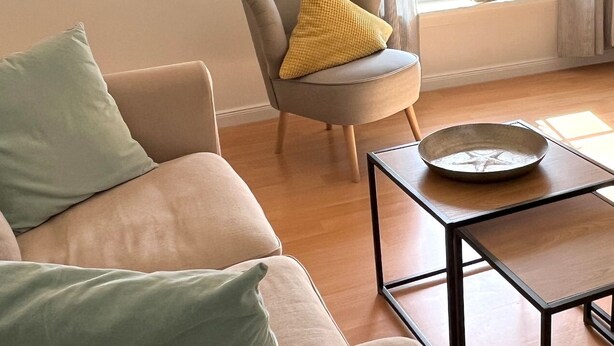 A living room with a sofa, a chair with a yellow pillow, a small table with a bowl, and a window with curtains. - Alter Konsumverein, App No. 2 - Your Comfortable Apartment at Alter Konsumverein (Sylt)