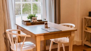A dining area with a wooden table, white chairs, a small plant, and a menu on the table. - Alter Konsumverein, App No. 2 - Your Comfortable Apartment at Alter Konsumverein (Sylt)