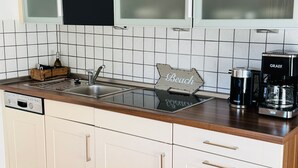 A kitchen with a modern design, featuring a stainless steel sink, a coffee maker, and a wooden sign on the countertop. - Alter Konsumverein, App No. 2 - Your Comfortable Apartment at Alter Konsumverein (Sylt)