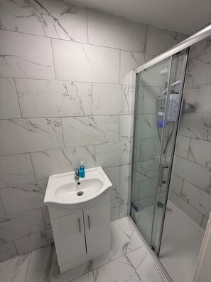 Ein Badezimmer mit einem weißen Waschbecken, Marmorfliesen, einer Duschkabine aus Glas und einem weißen Schrank.