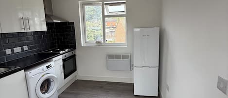 A compact kitchen with a washing machine, a built-in oven, and a window with a view of the outside.