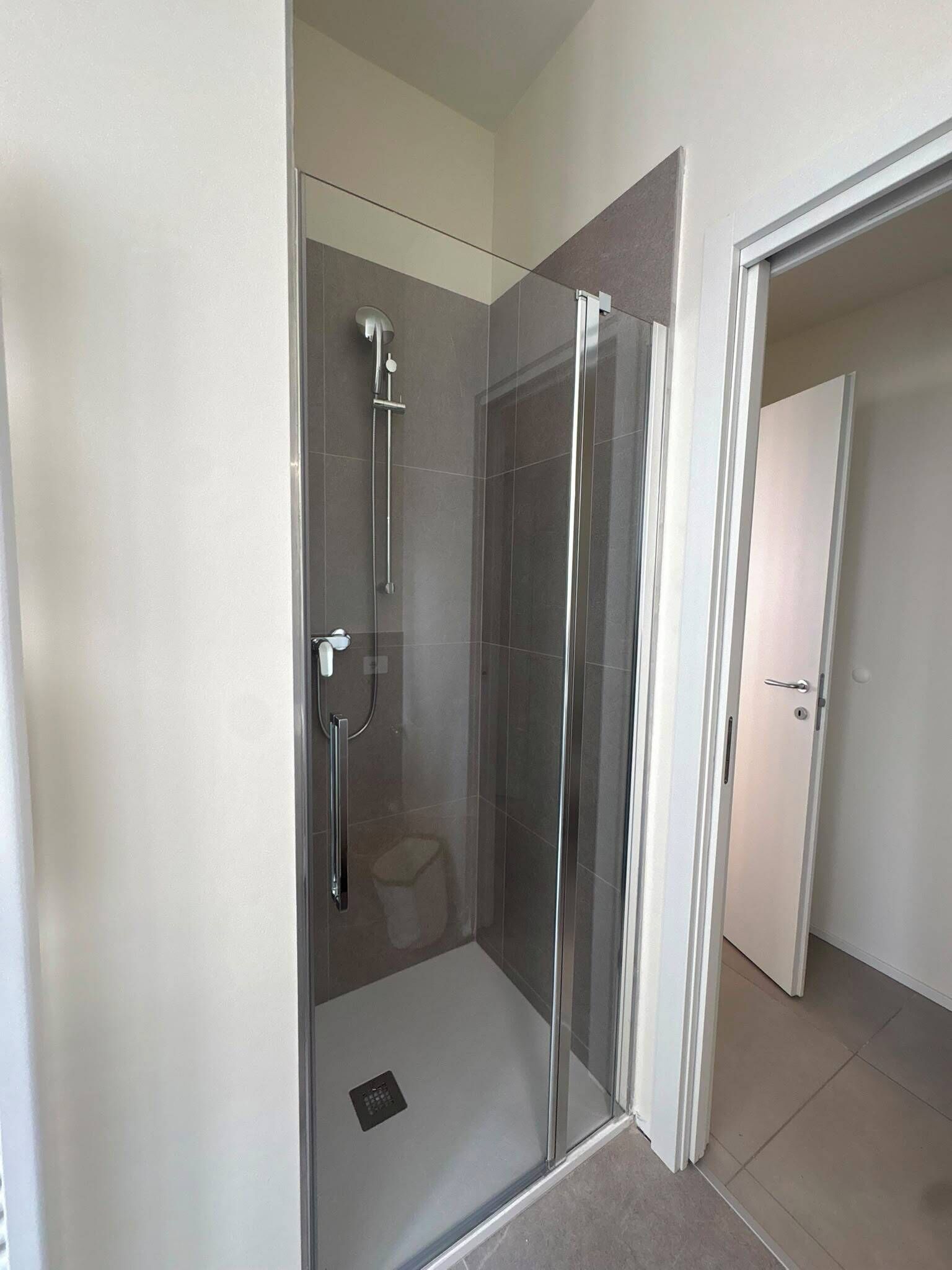 A modern bathroom with a glass-enclosed shower, a toilet, and a door leading to another room.
