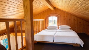 Quarto de cabana de madeira com cama no mezanino, uma janela com vista e corrimão de madeira.