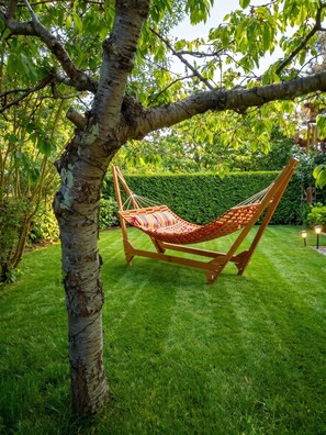 Eine Hängematte, die an einem Baum in einem gepflegten Garten befestigt ist, mit einer Hecke im Hintergrund.