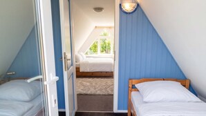 Ein Schlafzimmer mit zwei Einzelbetten, einer Tür zu einem anderen Raum und einem Fenster, das für natürliches Licht sorgt.